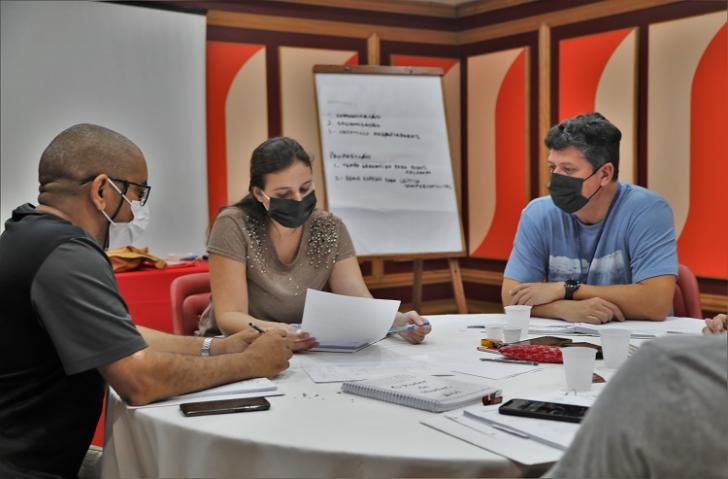 Foto de dois homens e uma mulher sentados a mesa estudando no curso Grid Liderança 