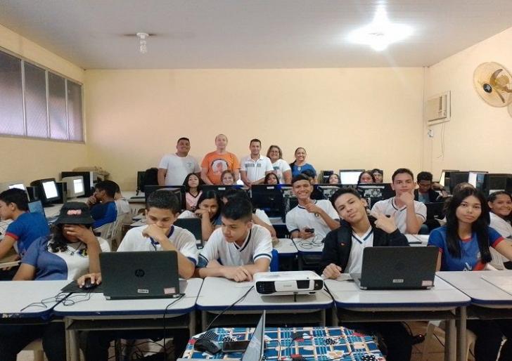 Ambiente de sala de informática com vários computadores e os alunos são crianças e adolescentes.