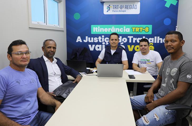 Fotografia em ambiente fechado que reúne cinco homens, em uma sala de audiência